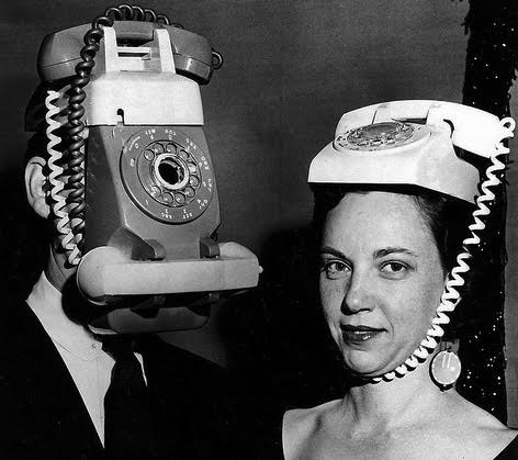 Black and white photograph of man and woman with old style phones attached to their heads.