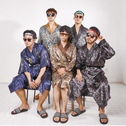Five men sitting together in night gowns, sunglasses, headbands, and slides.