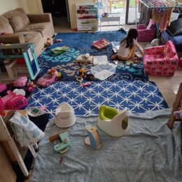 A family living room with children's toys and items including a potty, a child plays in the background